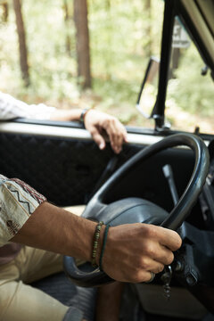 Close-up view of driver gripping steering wheel of a vehicle navigating through a forested area, showcasing detailed arm position and dashboard components