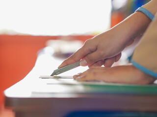 Closeup hand female using cutter to cut the paper in classroom at kid school. Lifestyle Concept...