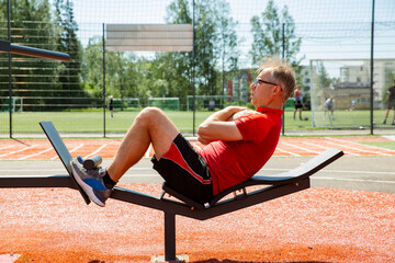 Man training on an adjustable abdominal bench. Targets core and abs. Outdoor workout improves core...