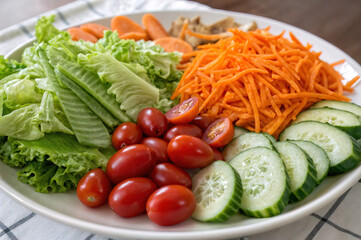 shows a plate of mixed vegetables, including shredded carrots, sliced cucumbers, cherry tomatoes, and lettuce. The vegetables are arranged neatly on a white plate.