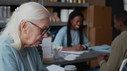 Tilt up shot of diverse volunteers in uniform providing work in food donation center - Powered by Adobe