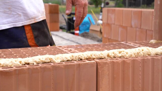 Worker applying adhesive foam to ceramic bricks during construction process