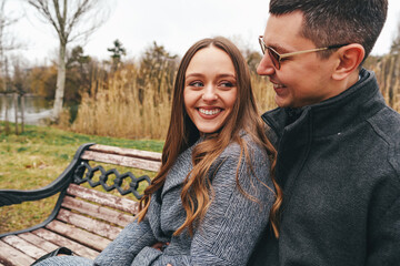 Couple enjoying each other's company on a park bench during a chilly autumn afternoon by the water