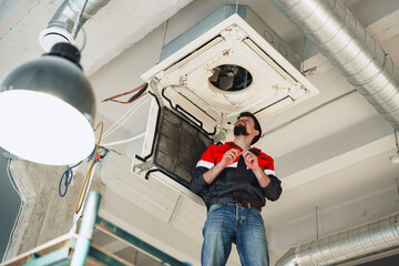 Technician repairs air conditioning unit in modern office space during daylight hours