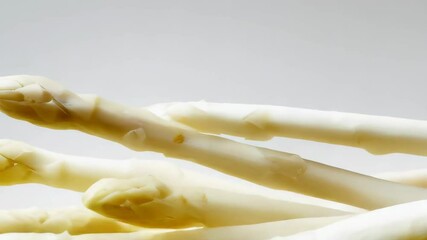 Close up of a cluster of several raw white asparagus spears with pointed tips on a bright white surface in a horizontal, still life food photography shot