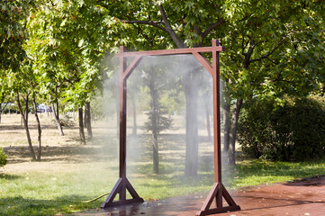 Water spray frame for cooling in hot weather on city street in Kyiv, Ukraine. Water mist cooling fog system in city park on hot summer. Protection against overheating and sunstroke by splashin