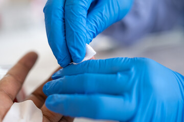Close-up of a healthcare worker wearing blue gloves cleaning a patient’s fingertip with cotton,...