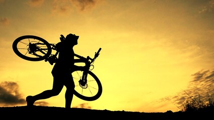 Obraz premium Cycling Adventure in the Dusk: Silhouette of a cyclist carrying his bike against a sunset, capturing the adventurous spirit and the peaceful transition of day to night.