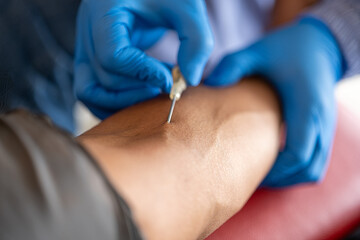 Close-up of a medical professional wearing blue gloves inserting a needle into a patient’s arm for a blood draw procedure in a clinical or laboratory setting.