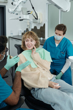 Happy Young Woman Touching Jaw While Talking to Dentist after Treatment Procedure