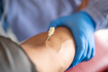 Close-up of a medical professional wearing blue gloves inserting a needle into a patient&rsquo;s arm for a blood draw procedure in a clinical or laboratory setting.