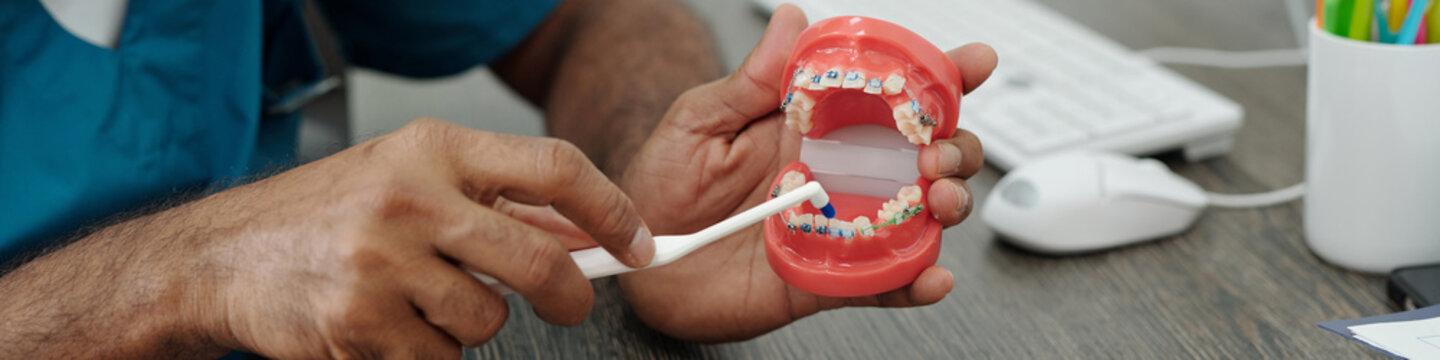 Mature Doctor Demonstrating How to Clean Teeth with Braces using Model