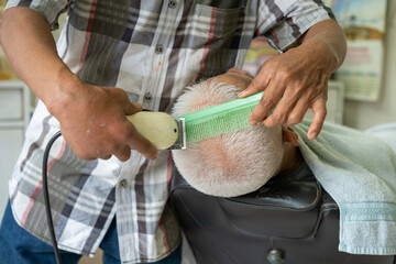 Close-up of a barber trimming an elderly man's white hair with electric clippers and comb, showcasing a traditional haircut session in a barbershop.