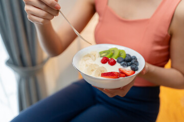 Young Asian Woman enjoying healthy cooking and enjoy eating Greek yogurt and fruits in kitchen after fitness and exercise at home.Asian lady eating yoghurt.nutritious,detox,healthy and diet concept
