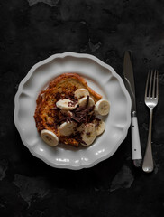 French toast with banana and chocolate chips - delicious breakfast, dessert, snack on a dark background, top view