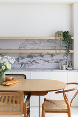 Bright modern dining room interior with wooden table and rattan chair positioned near kitchen area with marble backsplash creating an inviting space for peaceful moments at home