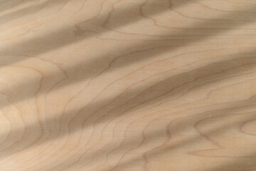 Light natural wood texture with fine grain provides warm surface background. Diagonal shadow pattern across wooden material creates abstract design, evoking feeling of organic material