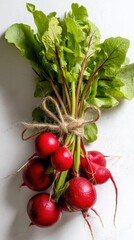 Fresh bunch of red radishes with green leaves tied with twine on white surface
