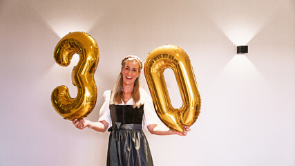 Bavarian woman with gold 30 balloons smiling during a birthday or festive anniversary event