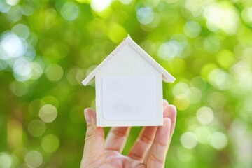 Dream home concept: hand holding miniature white house against green nature background