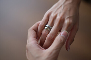 A close-up photograph captures two hands with intertwined fingers against a soft, blurred background. The image focuses on the delicate details of the hands, showcasing pale skin tones and visible ten