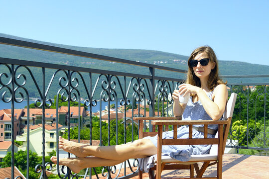 Portrait of a woman enjoying her holiday in a hotel located on the seashore: a female tourist drinks morning coffee on a terrace with a panoramic view. Vacation in Djenovici (Herceg Novi, Montenegro)