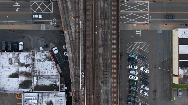 A top down, aerial view of the Long Island Railroad train tracks running through an industrial area on Long Island on a cloudy day. The camera is tilted straight down and slowly dolly in.