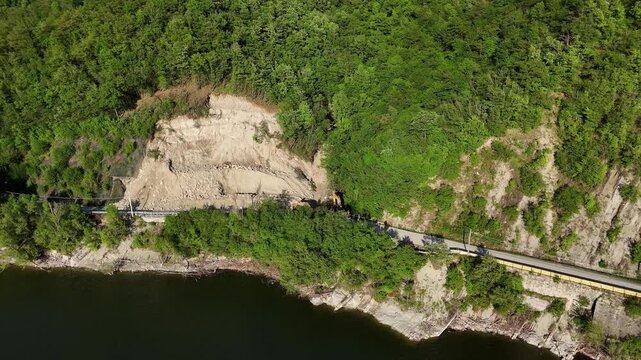 Drone shot of SP21 Vernasca after rockslide on April 22nd 2025, excavators operate to clear blocked road, surrounded by woodland and scattered rocks, real time