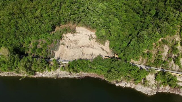 Drone shot of SP21 Vernasca after rockslide on April 22nd 2025, excavators operate to clear blocked road, surrounded by woodland and scattered rocks, real time