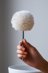 Fototapeta premium A person is holding a fluffy white brush with orange nails. The brush is white and has a pointed end. The person's nails are also orange, adding a pop of color to the scene