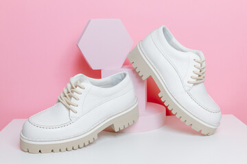 Pair of white leather lace up boots displayed on the podium with pink background, fashionable women footwear