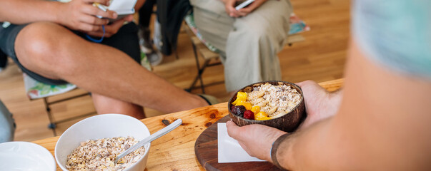 Banner of unrecognizable chef showing vegan breakfast bowl made with mango, banana, raspberries, cereals and muesli to audience taking notes in a cooking master class. Healthy cooking workshop concept