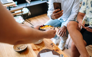 Unrecognizable chef showing healthy breakfast bowl made with mango, banana, raspberries, cereals and muesli to food bloggers and influencers taking photos with smartphones in cooking master class.
