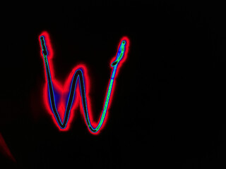 Glowing English letter W. On a black background with colored neon lines, a letter of the English alphabet is written by hand. The letter glows pink-red, creating a green-blue halo around it.