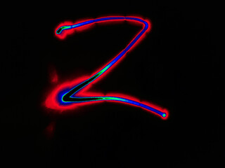 Glowing English letter Z. On a black background with colored neon lines, a letter of the English alphabet is written by hand. The letter glows pink-red, creating a green-blue halo around it.