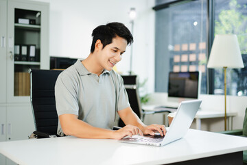 Fototapeta premium Asian man using laptop and tablet while sitting at her working place. Concentrated