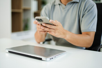 Hands of man using mobile phone in modern office with laptop and digital tablet