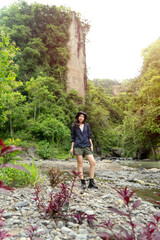 Naklejka premium Young Asian Woman Exploring Nature by a River in Hiking Gear During Outdoor Adventure