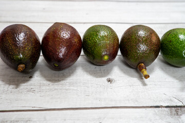 A fresh arrangement of whole and halved avocados displayed on a white wooden table, highlighting...