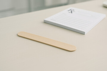Healthcare Essentials: A simple image of a medical wooden spatula and notepad in a medical clinic setting.