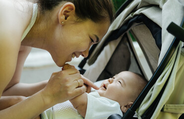 Young Asian mother is kissing cheeks of cute boy son with love and tenderness. Newborn baby cute and cheerful. Concept of motherhood parenting. 