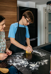 Teenage boy kneading dough with his mother in the kitchen