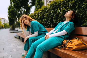 Healthcare workers take a break on a park bench during a busy shift, showcasing the challenges of...