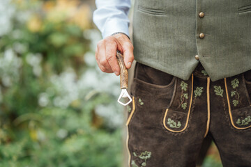 Detail of a man wearing lederhosen using a classic Bavarian knife as a bottle opener in Bavaria
