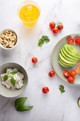 Top view of fresh and healthy breakfast with avocado, cherry tomatoes, ricotta, cashews and iced kombucha on a marble background. Concept of healthy food and minimalist aesthetics