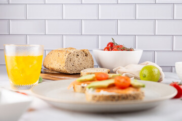 Toasts with avocado, salmon and cherry tomato in the foreground on a marble surface, with drink and bread in the background. Concept of nutritious breakfast and mindful living