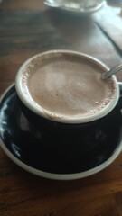 cup of coffee, A top-down view of a classic hot chocolate or coffee with beautiful white latte art in the shape of a stylized heart, resting on a rustic wooden table. The drink is served in a black
