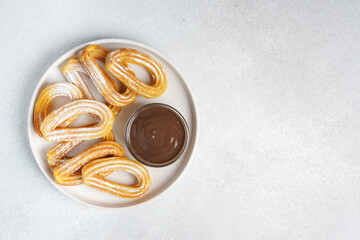 Traditional spanish dessert churros, fried dough pastry dusted with powdered sugar and chocolate sause on white background. Street food, sweet snack, homemade dessert. Top view, copy space