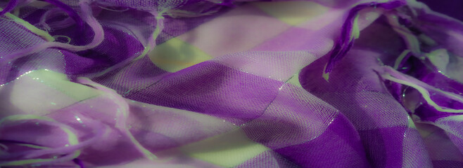 Blurred focus on shimmering purple and white fabric with layered textures and loose threads. The...