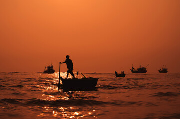 Silhouette of a Vietnamese male fisherman on round basket boat in sea in fishing village in the morning at sunrise in Vietnam
